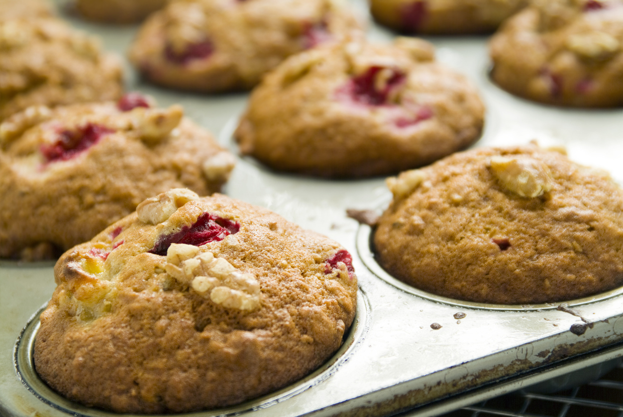 Une douzaine de muffins dorés, certains avec des fruits rouges et des noix, dans un moule.