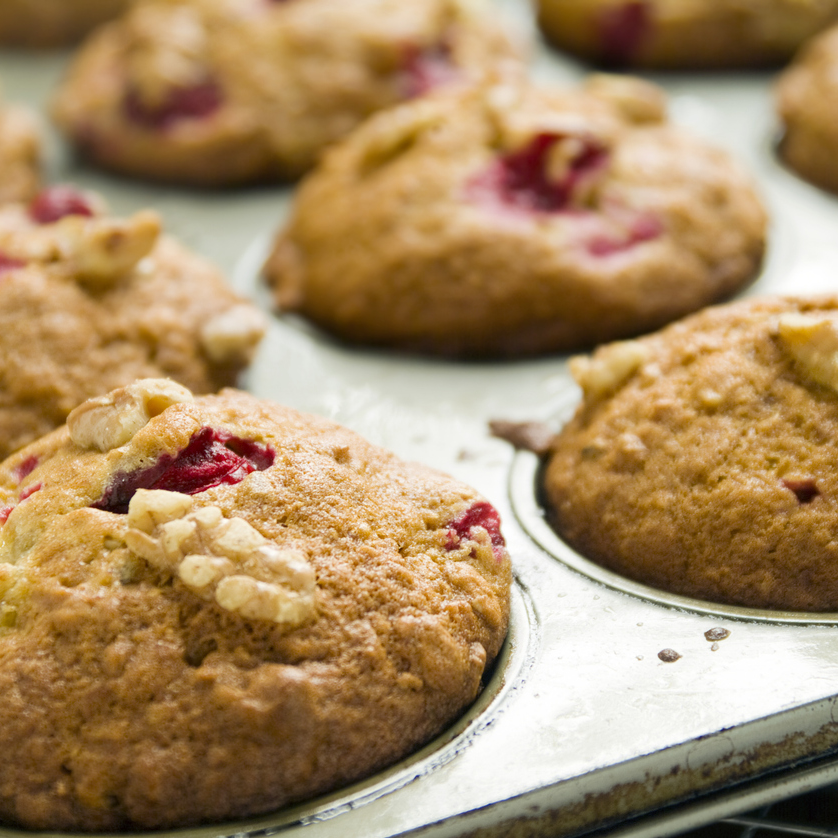 Une douzaine de muffins dorés, certains avec des fruits rouges et des noix, dans un moule.